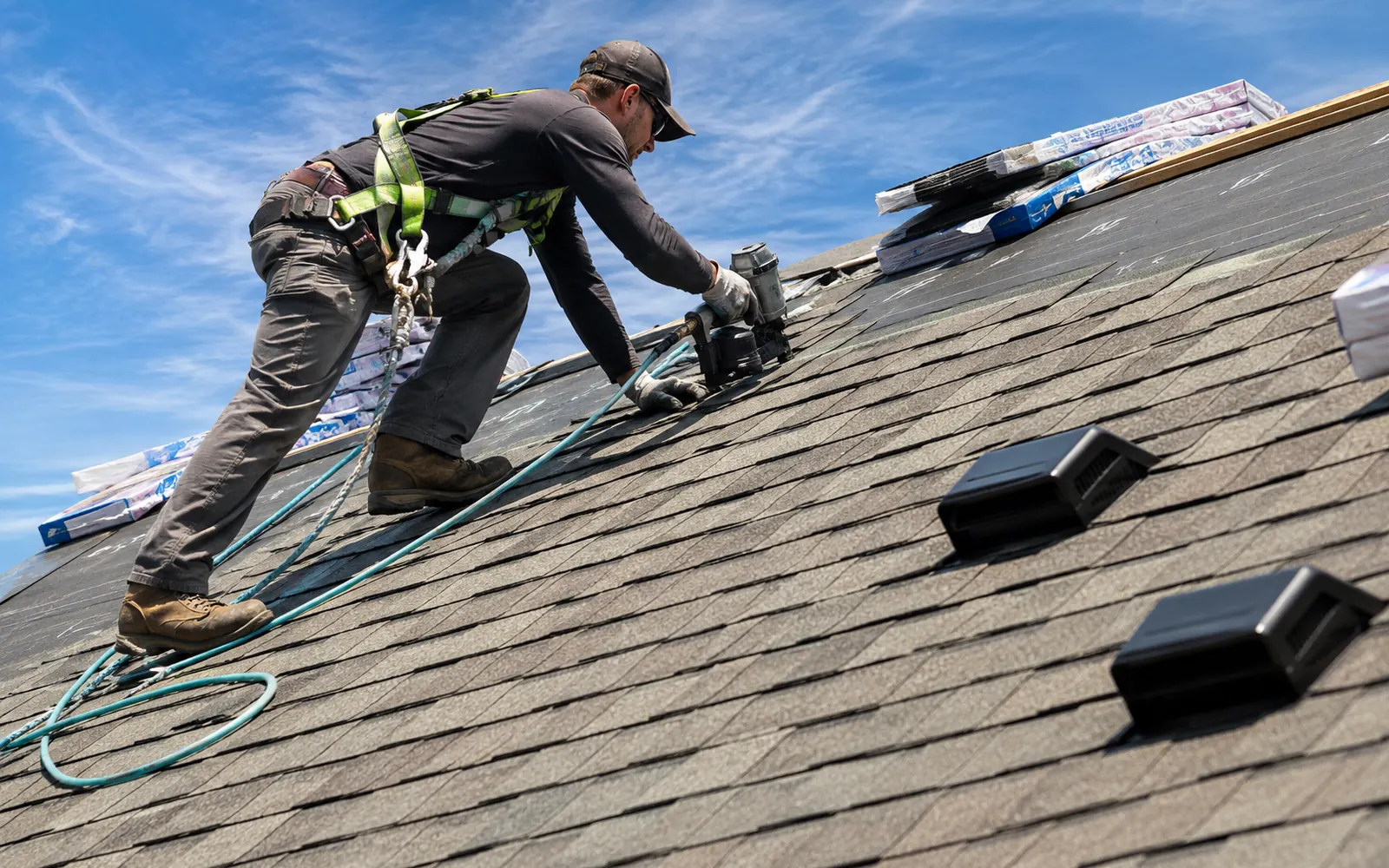Roofing contractor in a safety harness installing asphalt shingles on a residential roof